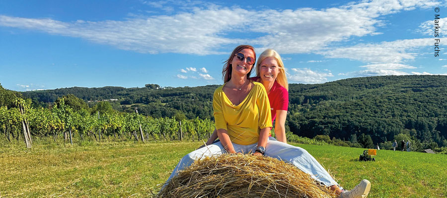 Foto vom Titelbild der aktuellen Ausgabe (zwei Frauen sitzen bei Sonnenschein und blauem Himmel auf einem Strohballen im Weingarten)