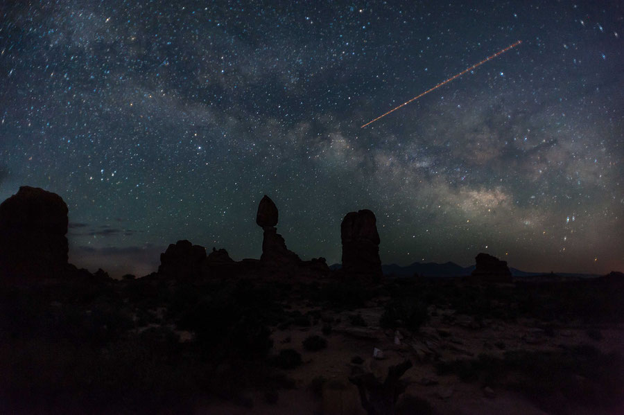 An Astrophotograph captured in Arches Nation Park in Utah, where rock formations are seen in the foreground and night sky with Milkyway in the background. International Space Station is passing in the sky leaving a trail of light.