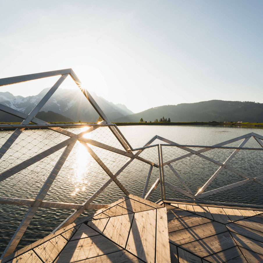 Sonnenaufgang am Prinzensee in Maria Alm mit Spiegelung der Berge im See und Aussichtsplattform – Familienwanderung am Hochkönig im Salzburger Land.