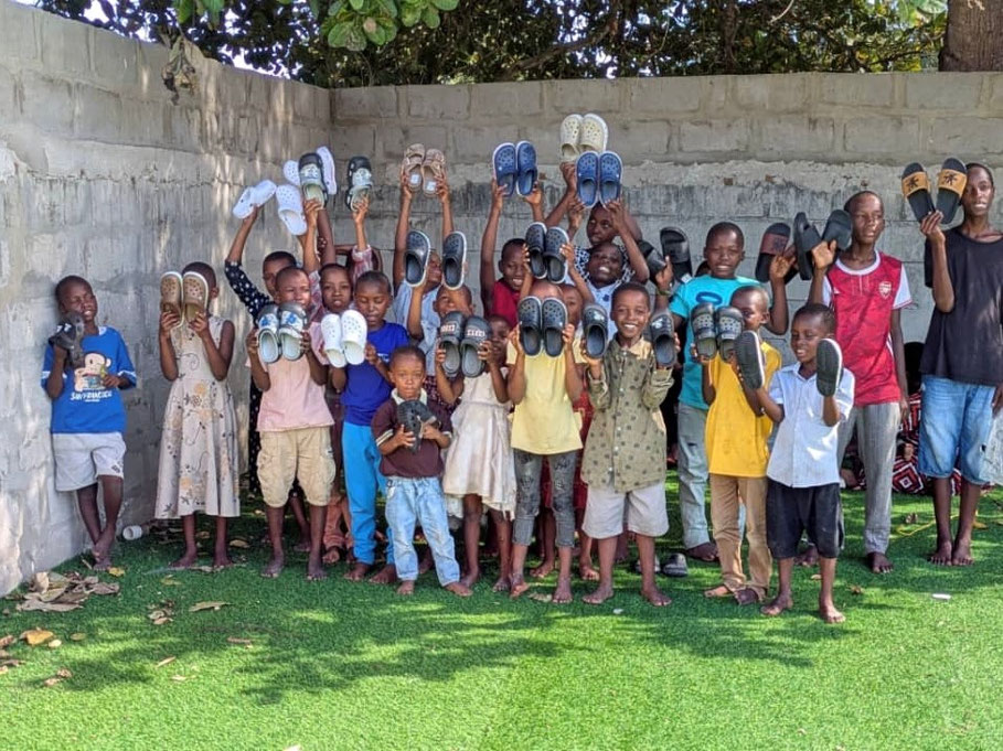 Gruppenbild von jungen Kindern, die jeweils stolz ein Paar Schuhe zur Kamera zeigen.