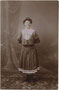 Junge Dame im Turnkostüm vor gemalter Hintergrundkulisse des Ateliers. Gelatinesilberabzug 9 x 14 cm. Impressum: Max Ketzler, Heiliggeiststraße 9, Innsbruck um 1905.  Inv.-Nr. vu914gs00859