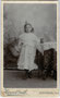 Erstkommunikantin vor bemalter Hintergrundkulisse im Photoatelier. Albuminabzug auf Untersatzkarton 6,6 x 10,6 cm (Visitformat), Rückseite blanko. Aufnahme: Heinrich Grüll, Schlanders im Vinschgau (Südtirol) um 1900.  Inv.-Nr. vuVIS-00083