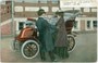 Ein Paar in Mänteln besteigt eine De Dion Bouton Voiturette 1902 in einer seltenen Version oder Sonderanfertigung als Vis-à-vis. Kombinationsfarbdruck 9 x 14 cm ohne Impressum wohl 1902.  Inv.-Nr. vu914kfd00042