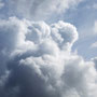 Ein Engel sitzt auf Wolken, mit angezogenen Beinen, am Rücken Engelsflügel, schaut nach links.