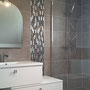 Frise murale de mosaïque de verre dans l'espace douche et à droite du meuble vasque. Présentation sous forme de plaque. Encadré par des profilés aluminium brillant.