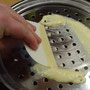 Teig in kleinen Portionen mit einem Teigschaber durch ein Spätzlesieb ins simmernde Kochwasser geben