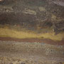 Das Freilegen der Kante offenbart archäologische Schichtungen: Unten eine seitliche Betonkante, darüber in rot die Trennschicht, dann gelber „fast neuer“ Sand und dann der gammelig verbrauchte Boden