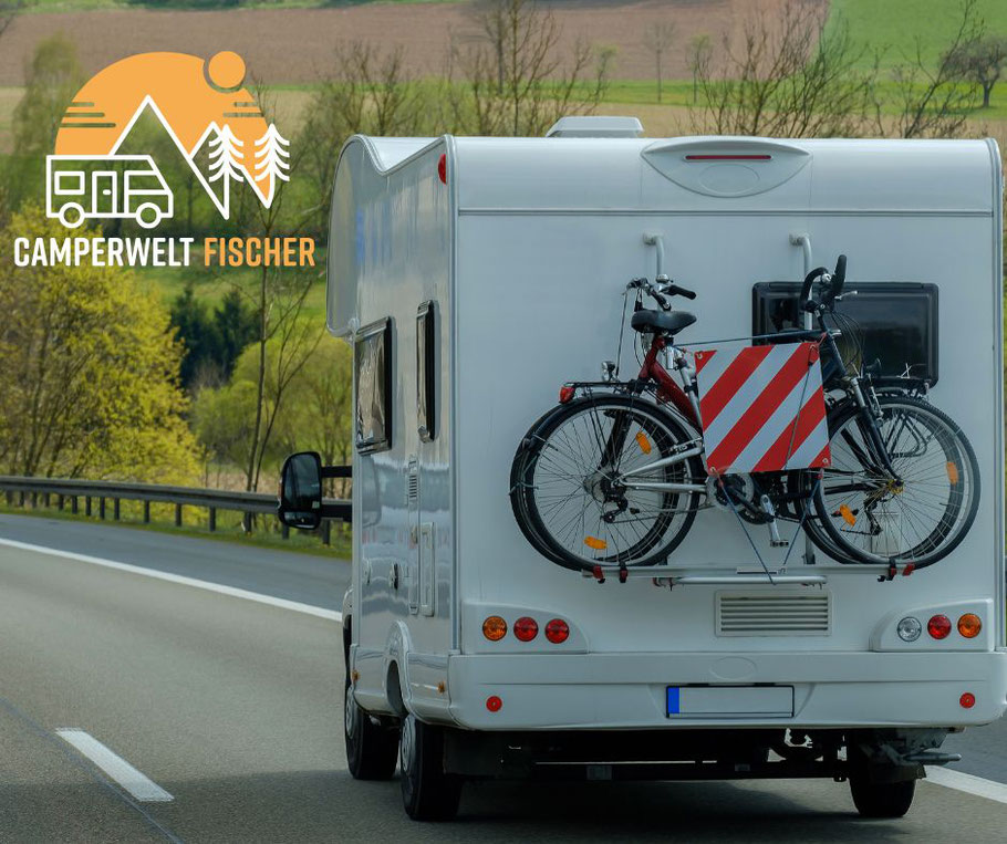 Camperwelt Fischer Wohnmobil mit Fahrrädern hinten, fährt auf einer Straße.