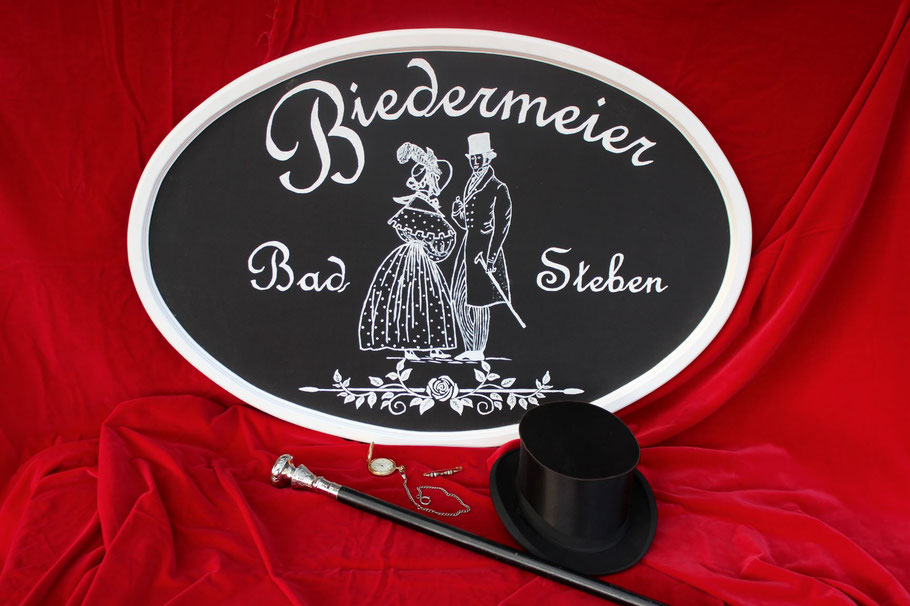 Unser Biedermeierschild (Biedermeier Bad Steben) mit Stock, Zylinder und Taschenuhr auf rotem Samt