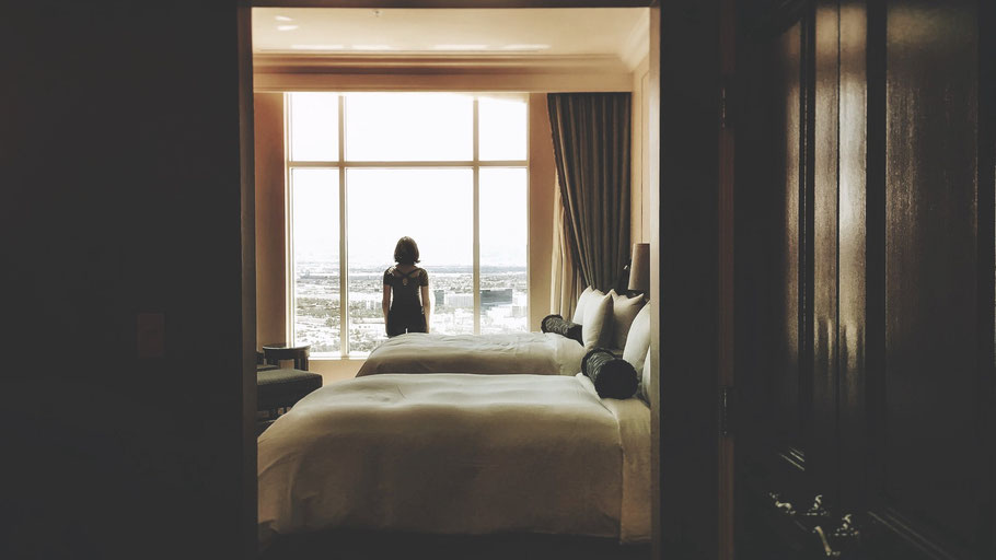 Frau schaut aus Hotelzimmer auf Stadt. Bild von Eunice Stahl auf Unsplash.
