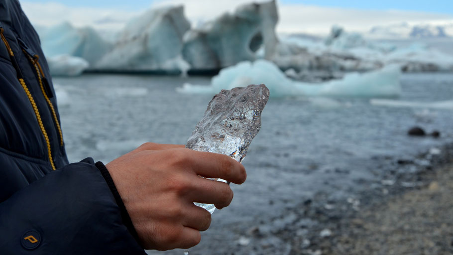 Mann mit Eisstück in der Hand vor Gletscher in Island. Bild von Agnieszka Bednarz auf Unsplash.