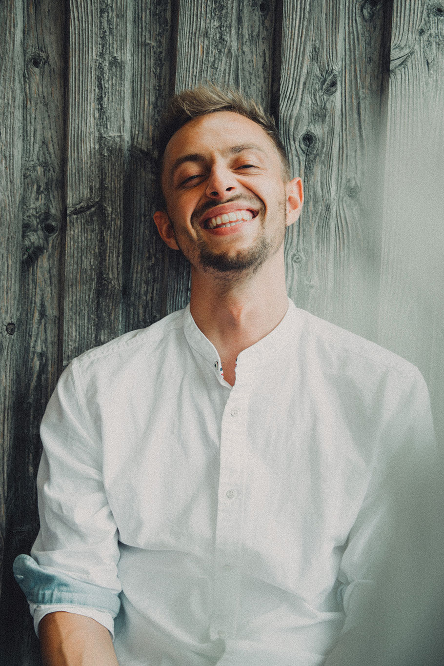 Pressefoto von Moritz Kruit: Der Musiker lächelt charismatisch vor einer Holzwand, während er für ein Foto posiert.