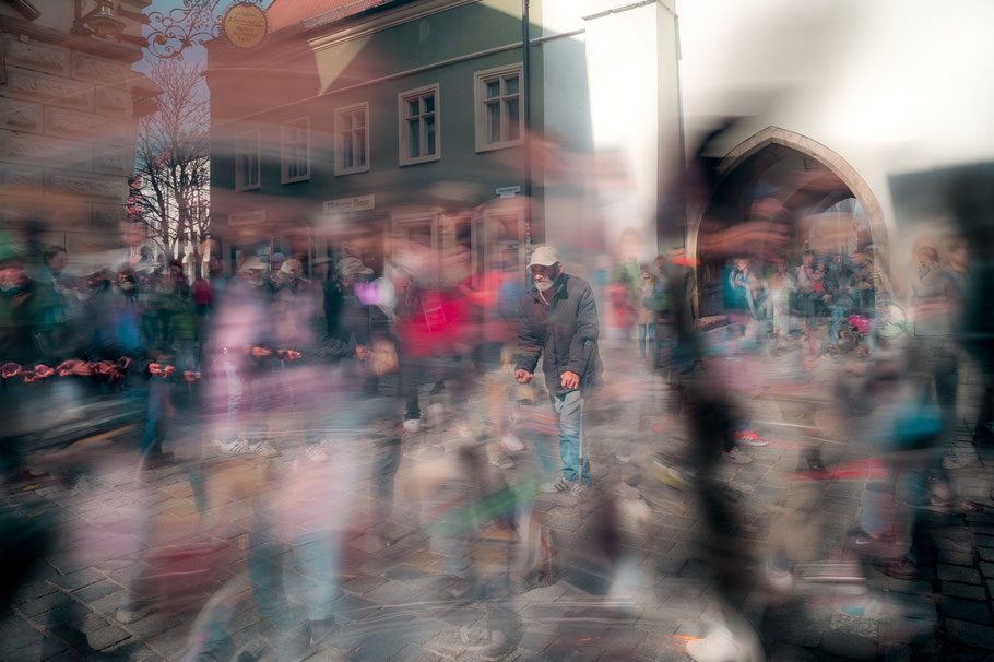 Mehrfachbelichtung und Komposition aus Langzeitbelichtungen mit Bettler in Straubing im Mittelpunkt. Sehr verschwommenes Porträt einer sich bewegenden Person. Künstlerische Langzeitbelichtung von Sebastian Schieder, Fotograf Regensburg.