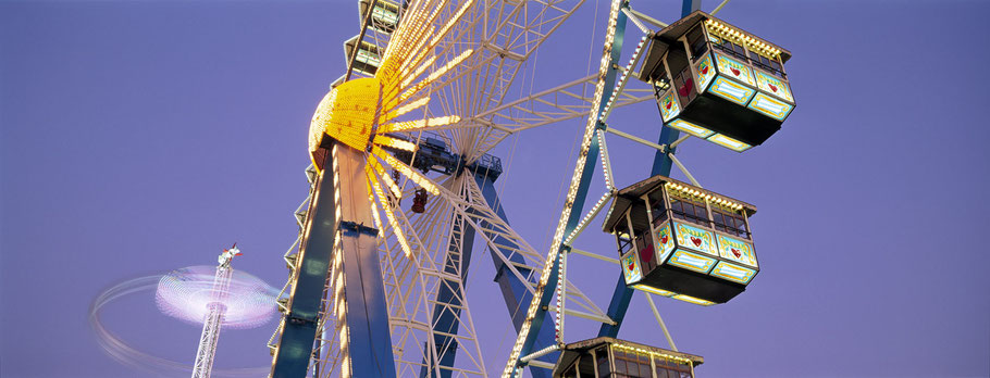 Nächtliche Aufnahme der Fahrgeschäfte auf dem Oktoberfest in München als Farbphoto im Panorama-Format