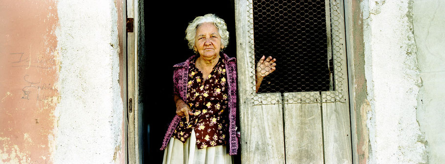 Alte kubanische Frau schaut in Trinidad d. Cuba aus der Haustür heraus, Farbphoto als Panorama-Photographie