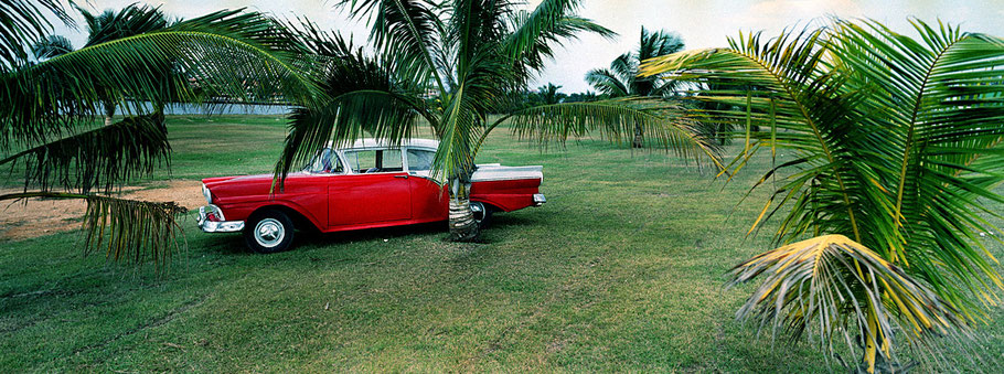 Roter Oldtimer auf der Wiese in Varadero als Farbphoto im Panoramaformat, Cuba