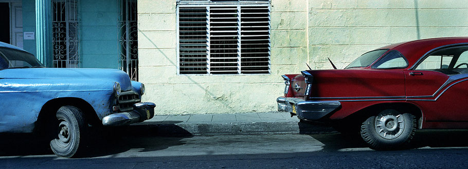 Roter und blauer Oldtimer auf der Straße in Santa Clara als Farbphoto im Panoramaformat, Cuba