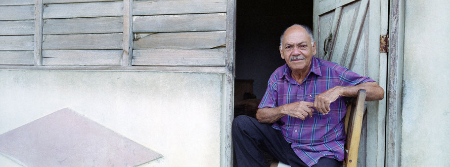 Alter Cubaner sitz im Eingang seines Hauses in Baracoa als Panorama-Photographie