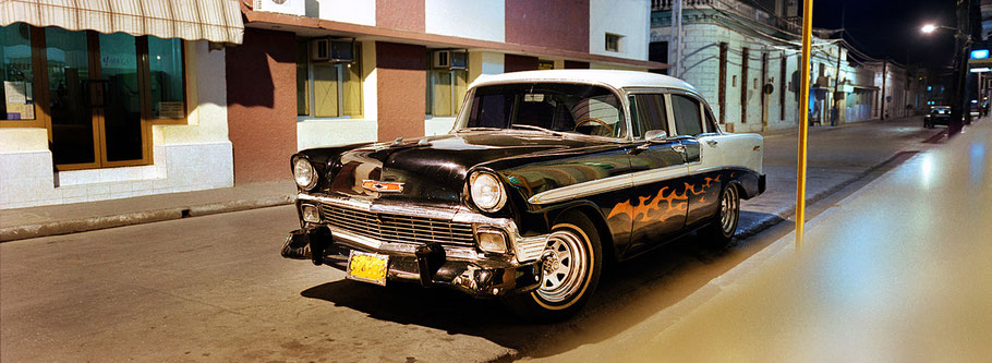 Schwarzer Oldtimer steht am Abend vor Häusern in Bayamo als Farbphoto im Panoramaformat, Cuba