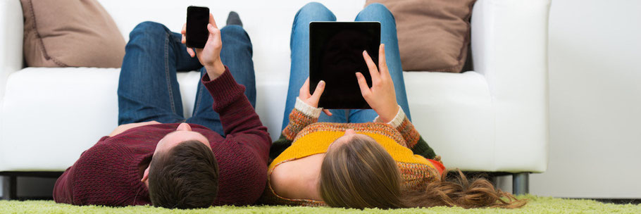 Highspeed Internet bis zum Sofa - zwei Personen surfen mit Smartphone und Tablet im Netz vom Sofa aus 