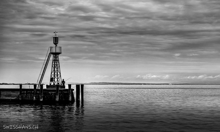 Ein Fischer steht beim Leuchtturm von Rorschach