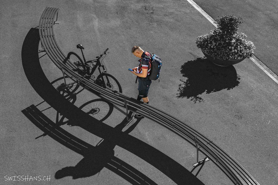 Radfahrer mit Mountainbike bei einer Parkbank schau auf sein Smartphone