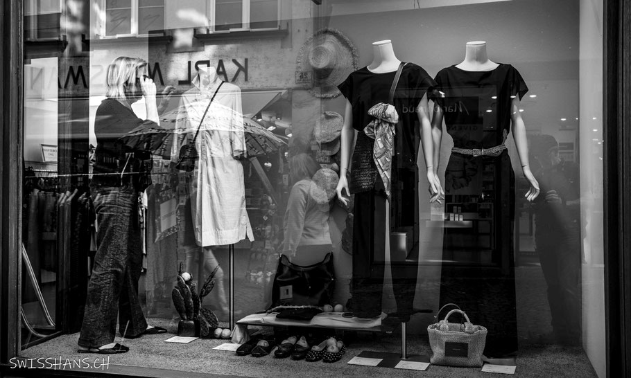 Eine Verkäuferin steht im Schaufenster und schaut sich die Schaufensterpuppe genau an.