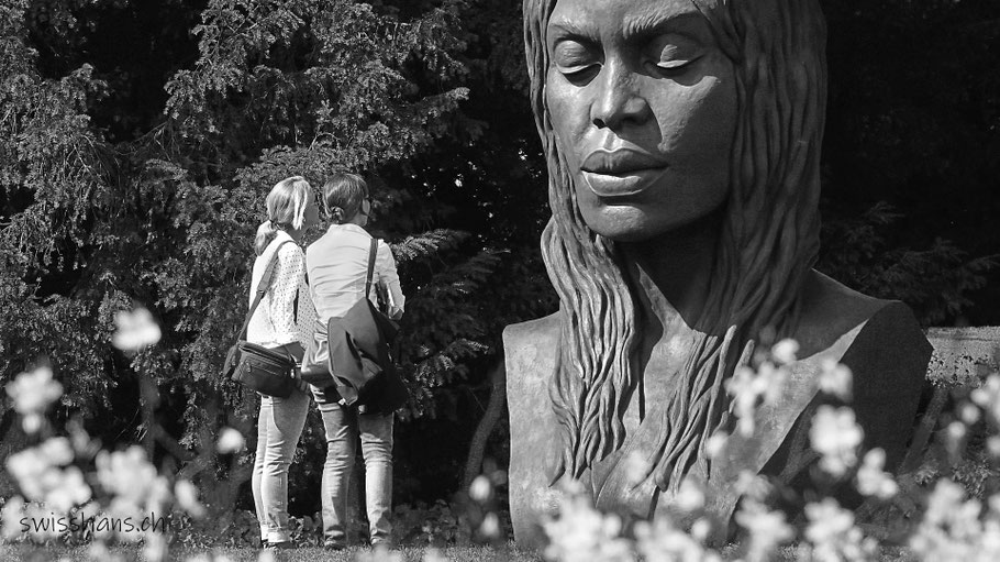 Zwei Frauen stehen vor einer Skulptur einer Frau an der Skulpturenausstellung BadRagartz in Bad Ragaz