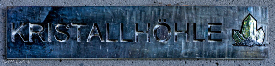 Metalltafel mit der Aufschrift Kristallhöhle und einem Kristall an der Wand des Eingangs zur Kristallhöhle Kobelwald