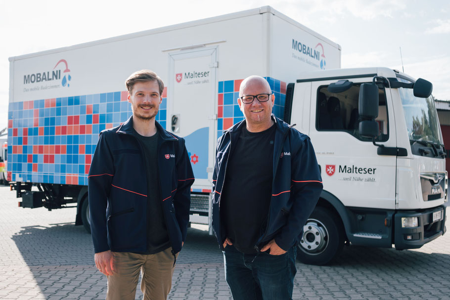 Projektkoordinator Julian Wundke (links) und Sven Pfeiffer, technischer Leiter, vor dem Zugfahrzeug von MOBALNI; Bildquelle: Mieres/Malteser