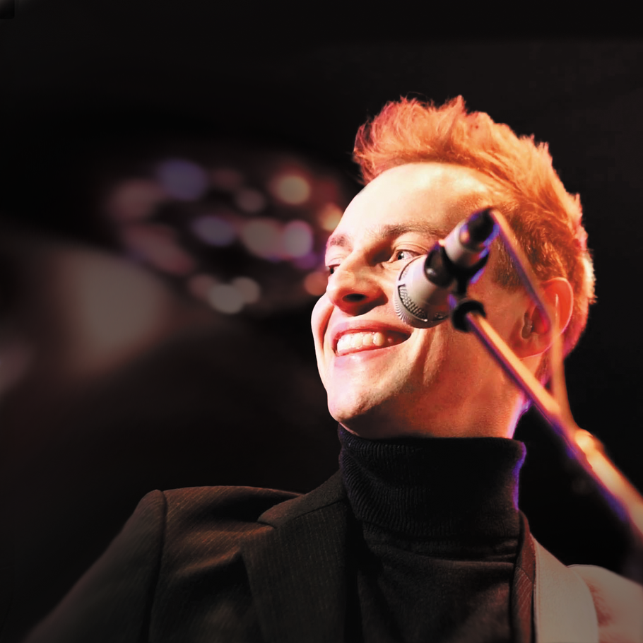 „Sänger Moritz Kruit lächelnd auf der Bühne im Birdland Hamburg mit Mikrofon während eines Live-Auftritts“