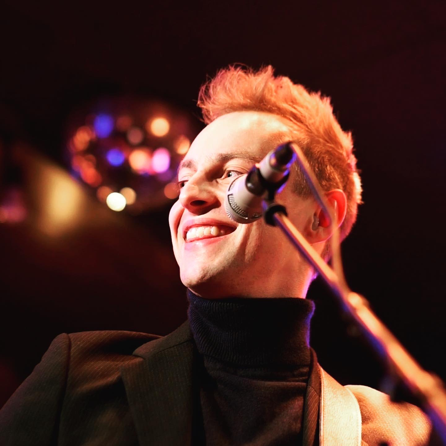 Moritz Kruit auf der Bühne im Birdland Hamburg: Der Musiker mit Gitarre und Mikrofon strahlt charismatisch lächelnd während eines Live-Auftritts.