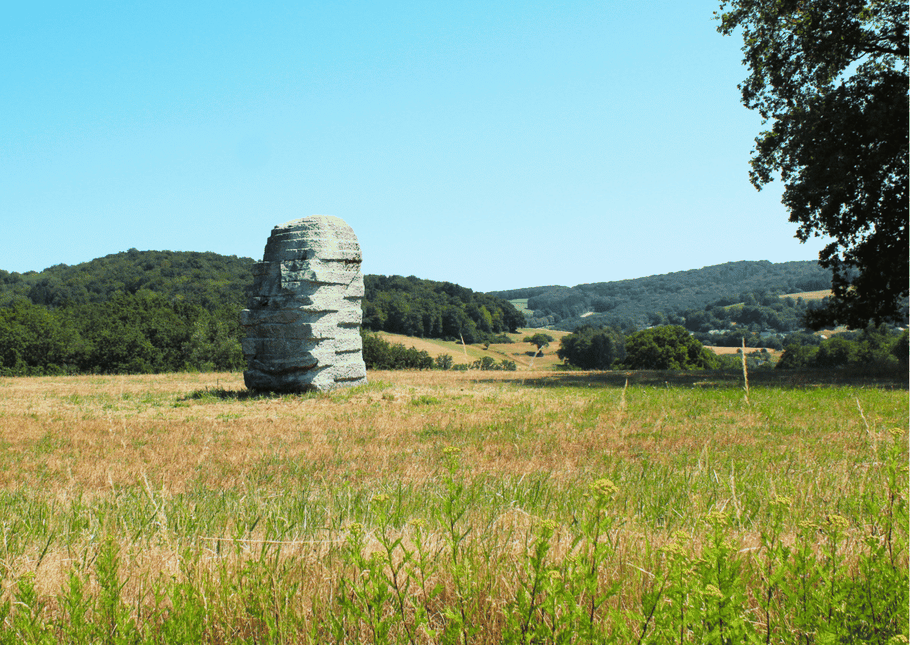 Eine monumentale Skulptur aus hellem Sandstein steht auf einer grünen Wiese unter blauem Himmel auf der Baltersweiler Höhe bei St. Wendel