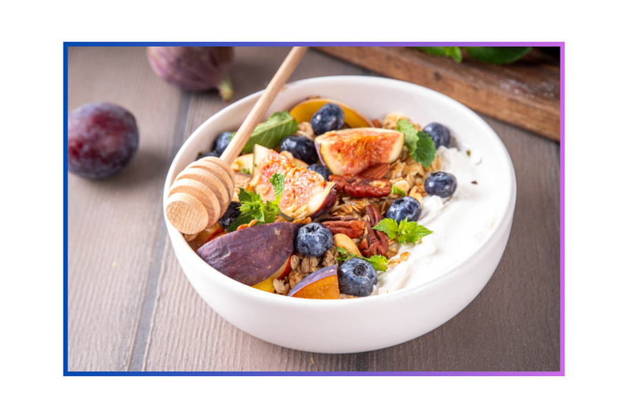 Eine weiße Schüssel mit Joghurt, frischem Obst und Nüssen steht auf einem Tisch