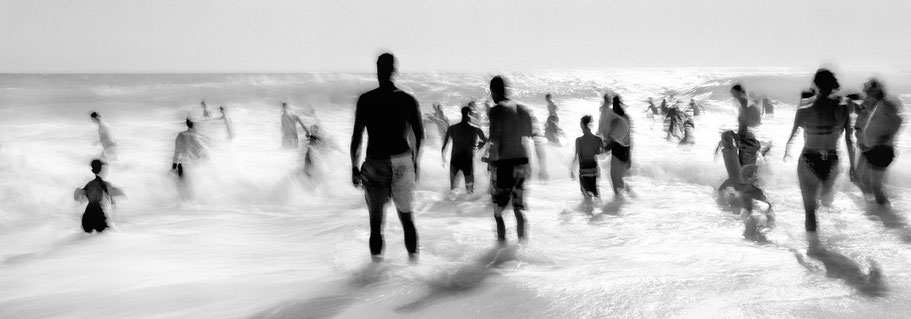 Menschen trotzen den Wellen des Atlantiks als schemenhafte Langzeitbelichtung in schwarz-weiß als Panorama-Photographie