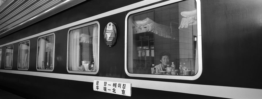 Frau schaut aus dem Abteil im Zug von Peking nach Pyongyang, Nord Korea, in schwarz-weiß als Panorama-Photographie