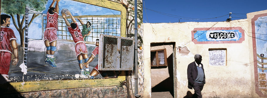 Eingang zum Basketballfeld mit Mann in Asmara, Eritrea, als Farbphoto im Panorama-Format