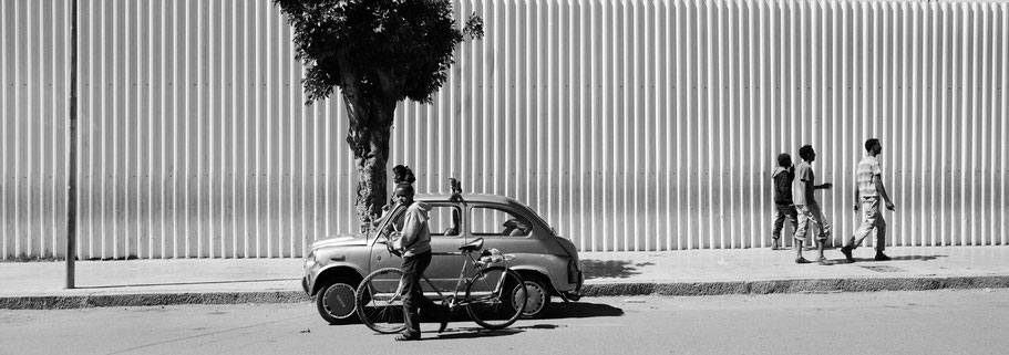 Junge Männer in der Mai Bela Avenue in Asmara, Eritrea, als Schwarzweißphoto im Panorama-Format