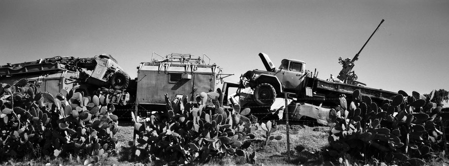 Kriegsschrott aufgetürmt als Mauer im Tank Graveyard in Asmara, Eritrea, als Schwarzweißphoto im Panorama-Format