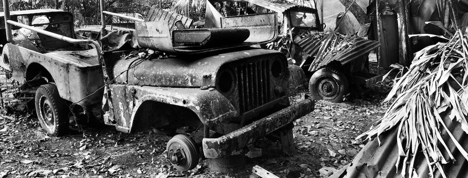 Reste von Oldtimer-Jeeps bei Marari in Kerala , Indien, als Schwarzweißphoto im Panorama-Format