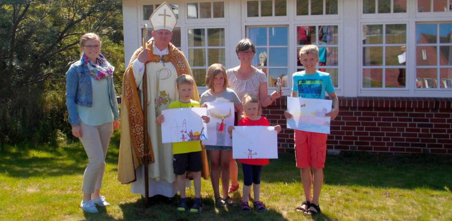 Der heilige Nikolaus und Pastoralreferentin sowie  Insel-Seelsorgerin Susanne Wübker umrahmt von Kindern, die selbstgemalte Bilder in der Hand halten.