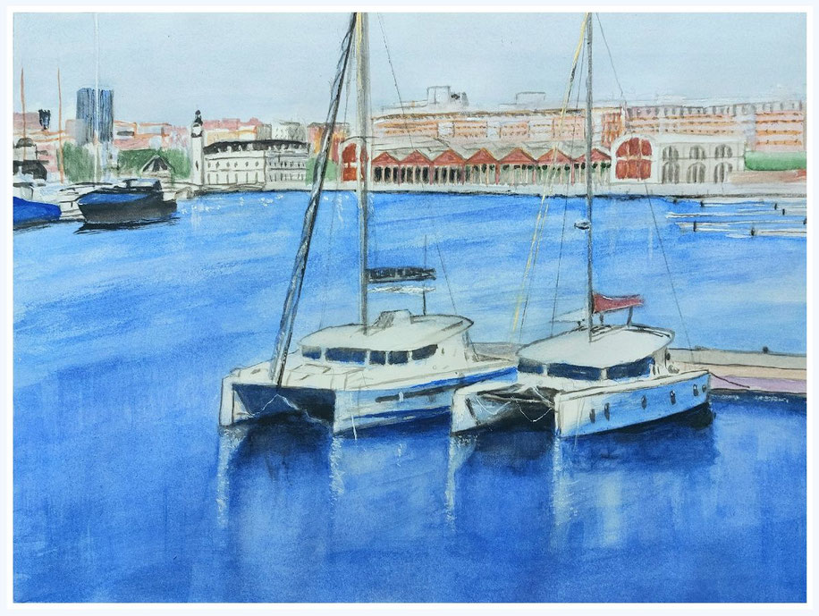 Catamaranes amarrados en el puerto de Valencia, con edificios portuarios y reflejos sobre el agua tranquila.