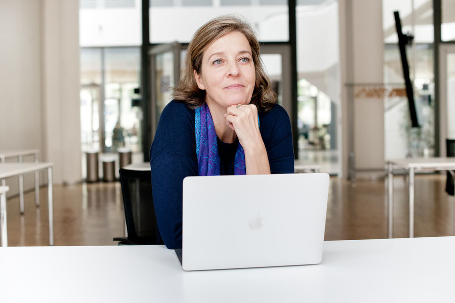Kirstin, Expertin für Taschengeld und Finanzbildung, lächelt in ihrem Büro am Schreibtisch mit Computer, bereit, Eltern bei der Einführung von Taschengeld für Schulkinder zu beraten.