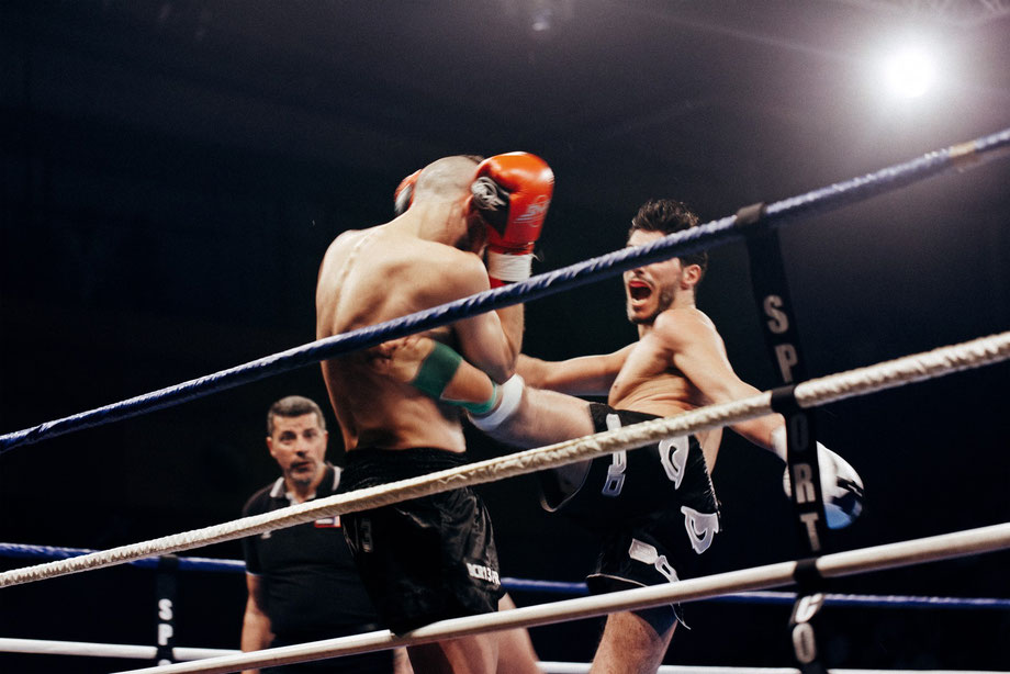 Zwei Muay Thai-Kämpfer kämpfen im Boxring. Der Kämpfer mit den schwarzen Handschuhen tritt den Kämpfer mit den orangen Handschuhen.