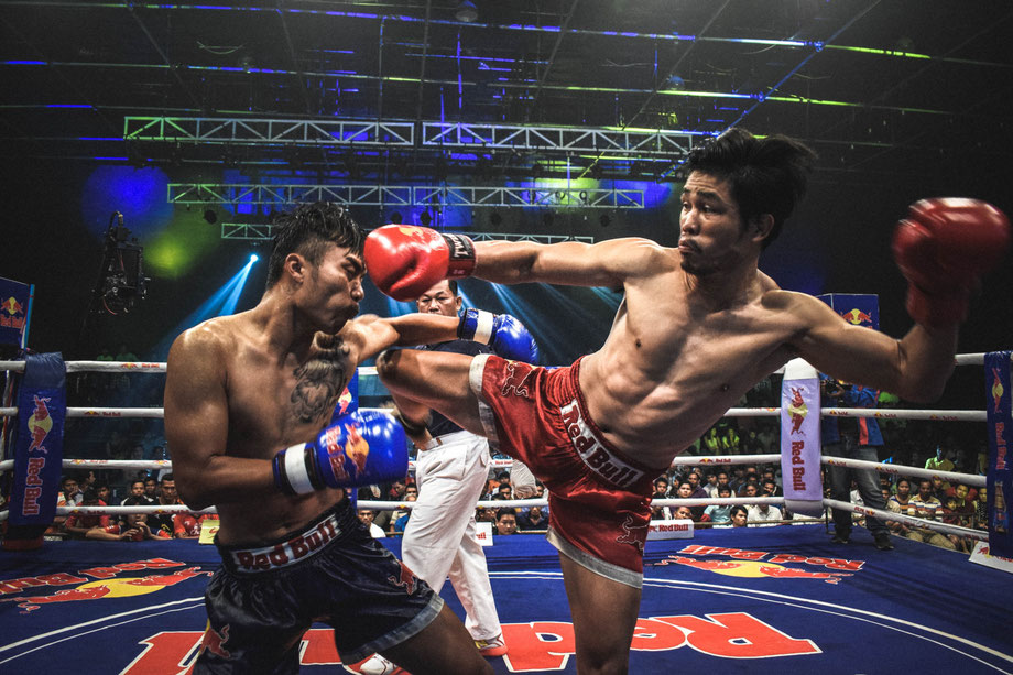 Zwei Muay Thai-Kämpfer im Boxring. Der Kämpfer in der roten Hose tritt den Kämpfer in der schwarzen Hose.
