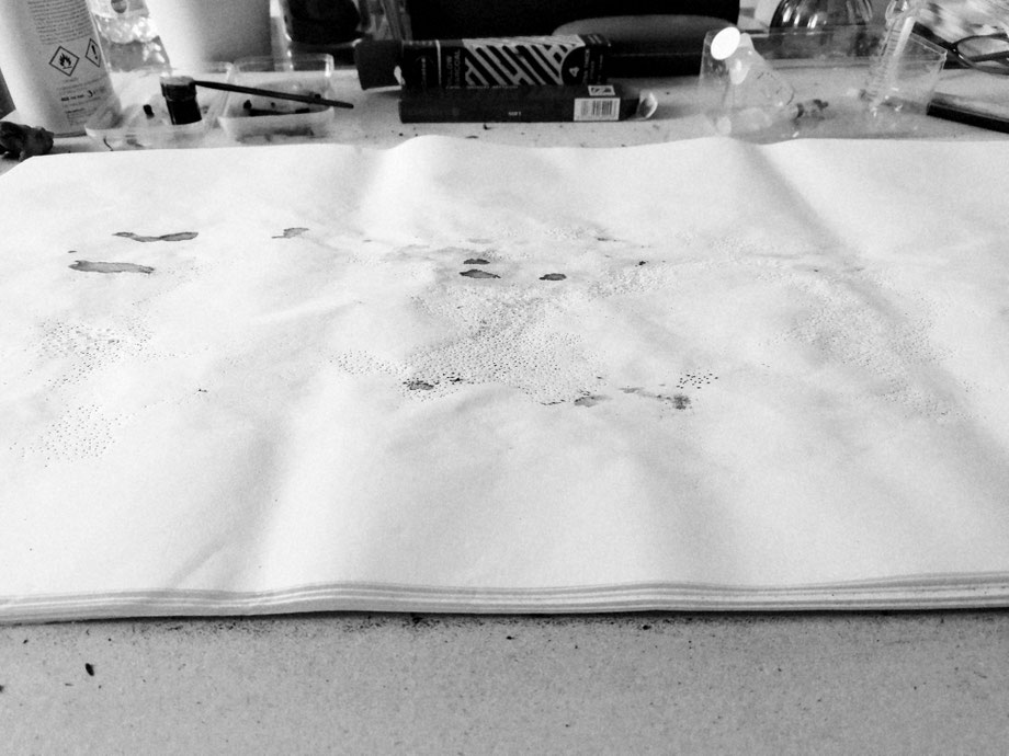 à vau-l’eau 2023, vue d’ensemble : photographie de la rame de papier en cours de transformation, les outils et les effets des interventions successives (eau, encre, pointe sèche).