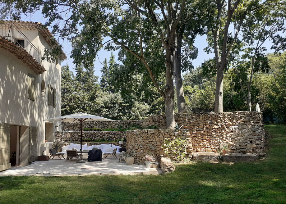 Rénovation, extension et surélévation d'une maison à Aix-en-Provence. Jardin dont la terrasse avec une banquette sur mesure, murs de restanques en pierres apparentes