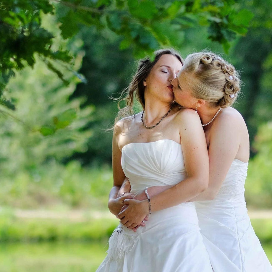 hochzeitsfotograf NRW, fotoshooting hochzeit NRW, zwei bräute in weißen brautkleidern küssen sich in einem park