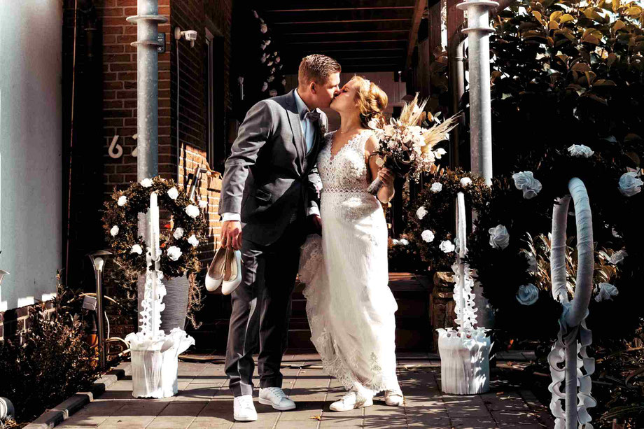 hochzeitsfotograf sendenhorst, fotoshooting hochzeit sendenhorst, braut und bräutigam stehen küssend vor einem für die hochzeit traditionell geschmückten haus