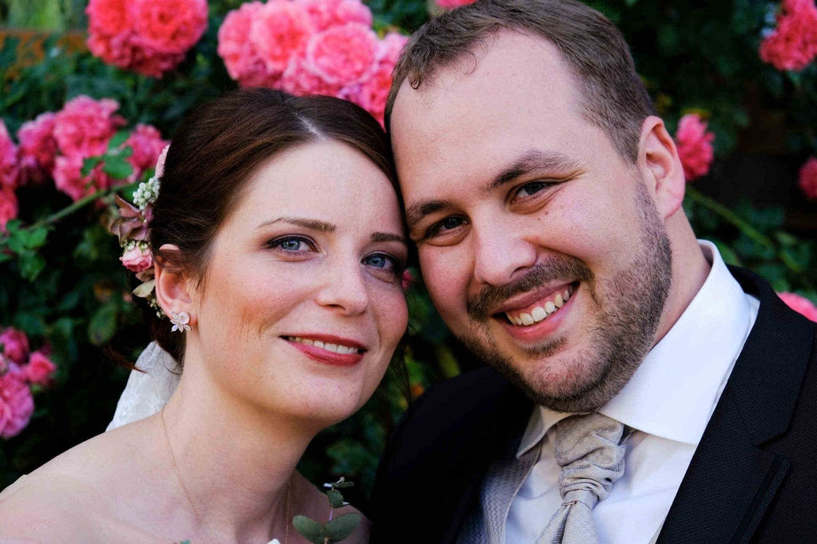 hochzeitsfotograf beverungen, braut und bräutigam lächeln in die kamera - rote rosen im hintergrund